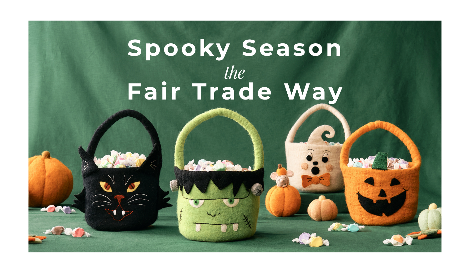 Three Halloween-themed felt baskets filled with candy are displayed against a dark green backdrop with the text 'Spooky Season the Fair Trade Way' above them. The baskets are shaped like a black cat, a green monster, and a white pumpkin, with small orange pumpkins and candy scattered around.