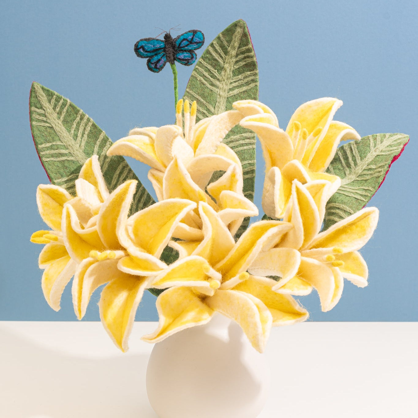Yellow flowers in a white vase with green leaves and a blue butterfly on a light blue background